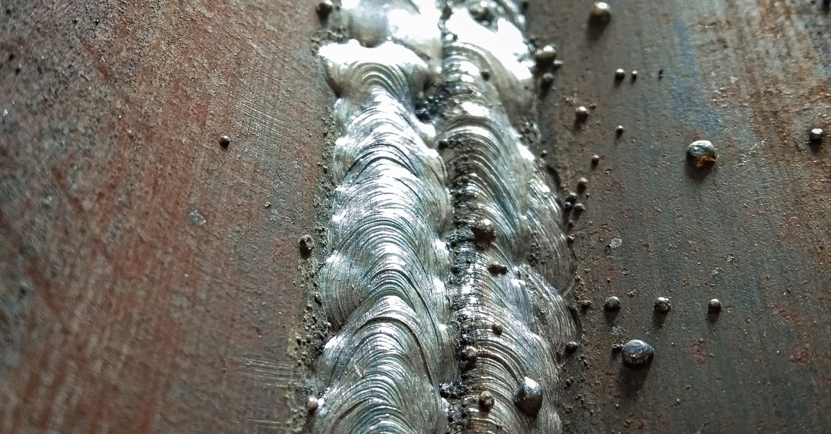 A steel surface shows flux residue with visible ridging and scattered raised bumps across the textured area.