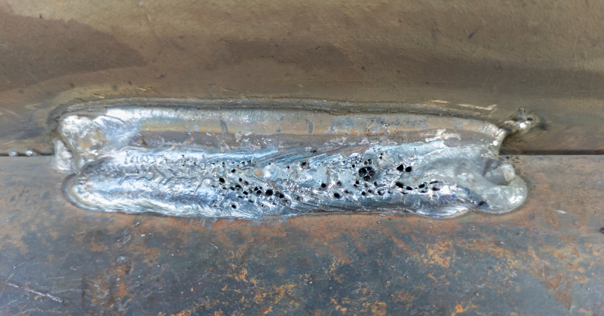 A welded metal surface shows a visible cavity in the weld bead, marked by porosity or a wormhole-like defect.