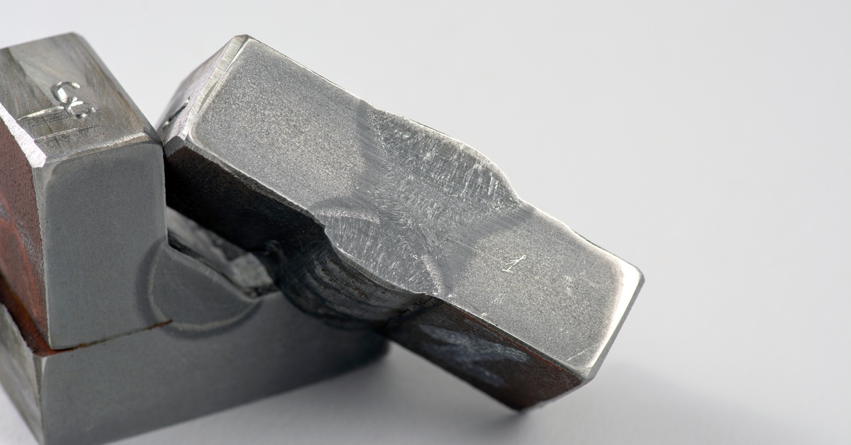Two metal pieces display a macro-etched cross-section of a butt weld joint with visible penetration and fusion lines.